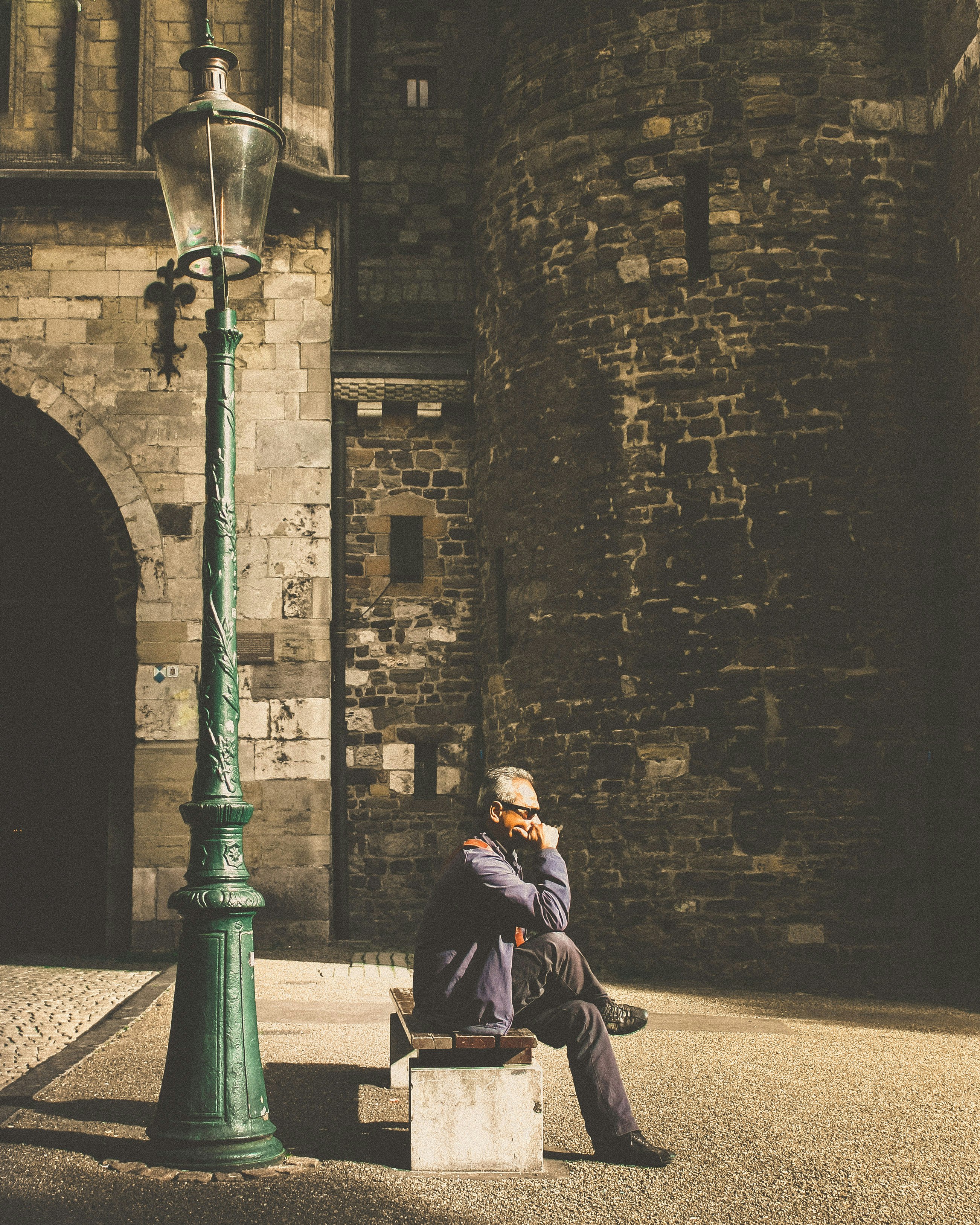 man sitting on bench beside post lamp